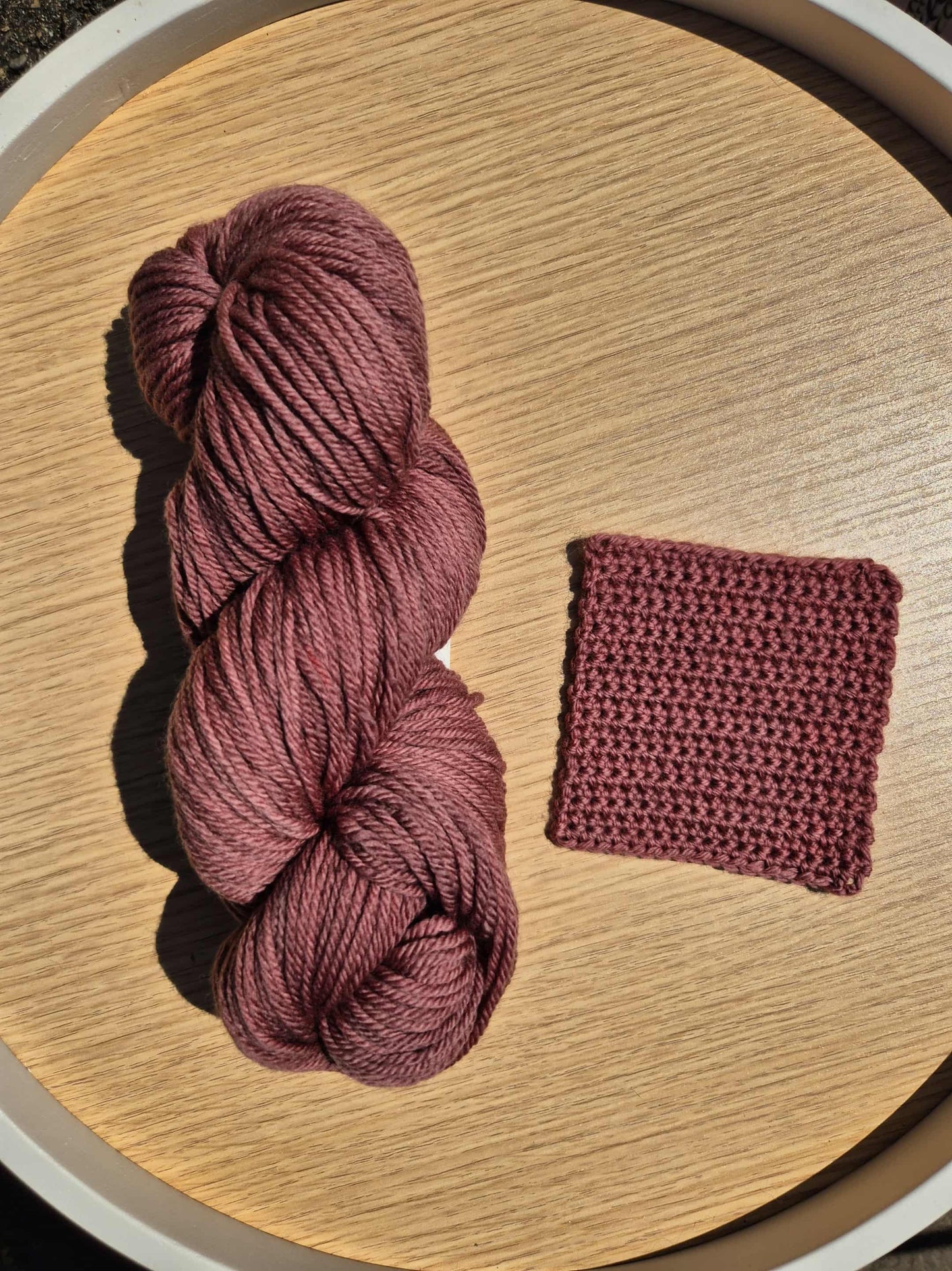 Red Wine coloured skein of yarn and a small crochet swatch on a wooden surface