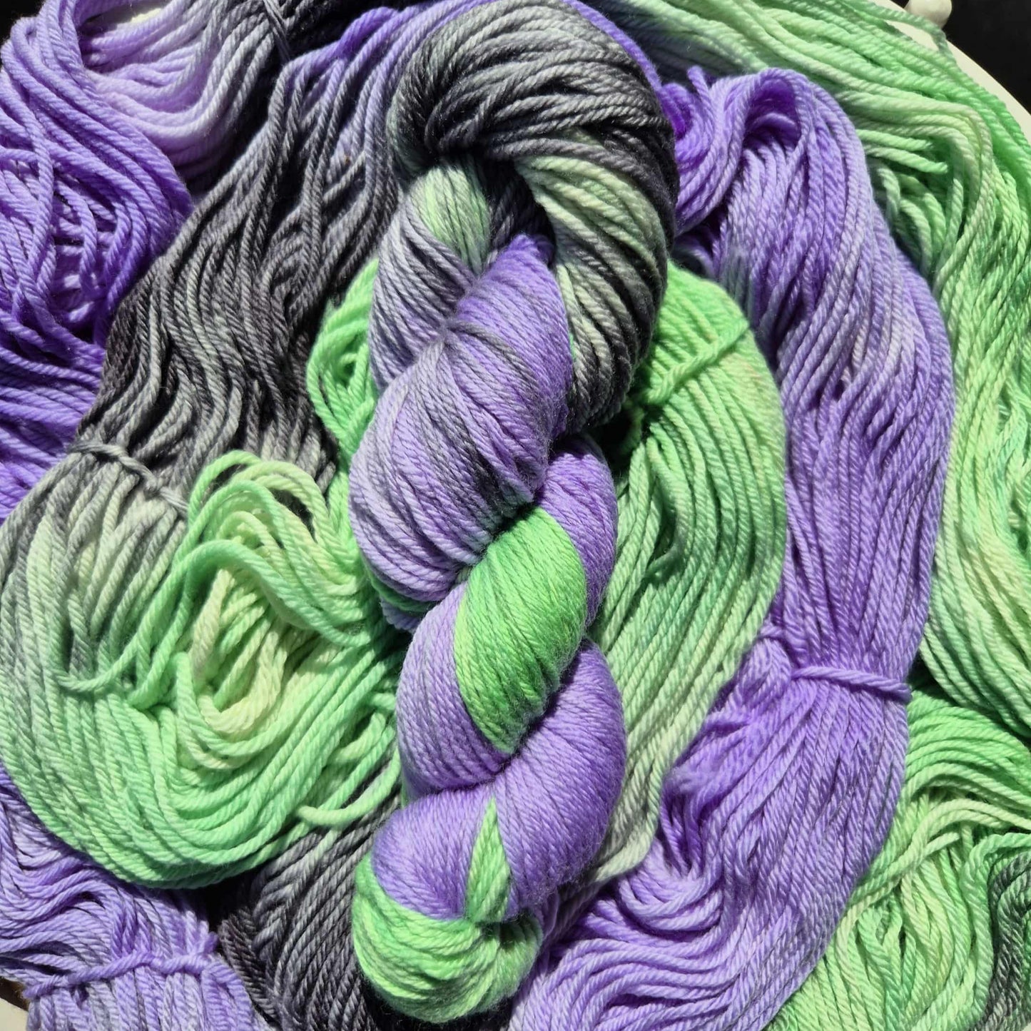 Multi-coloured yarn skeins in green, purple, and black on a white surface.