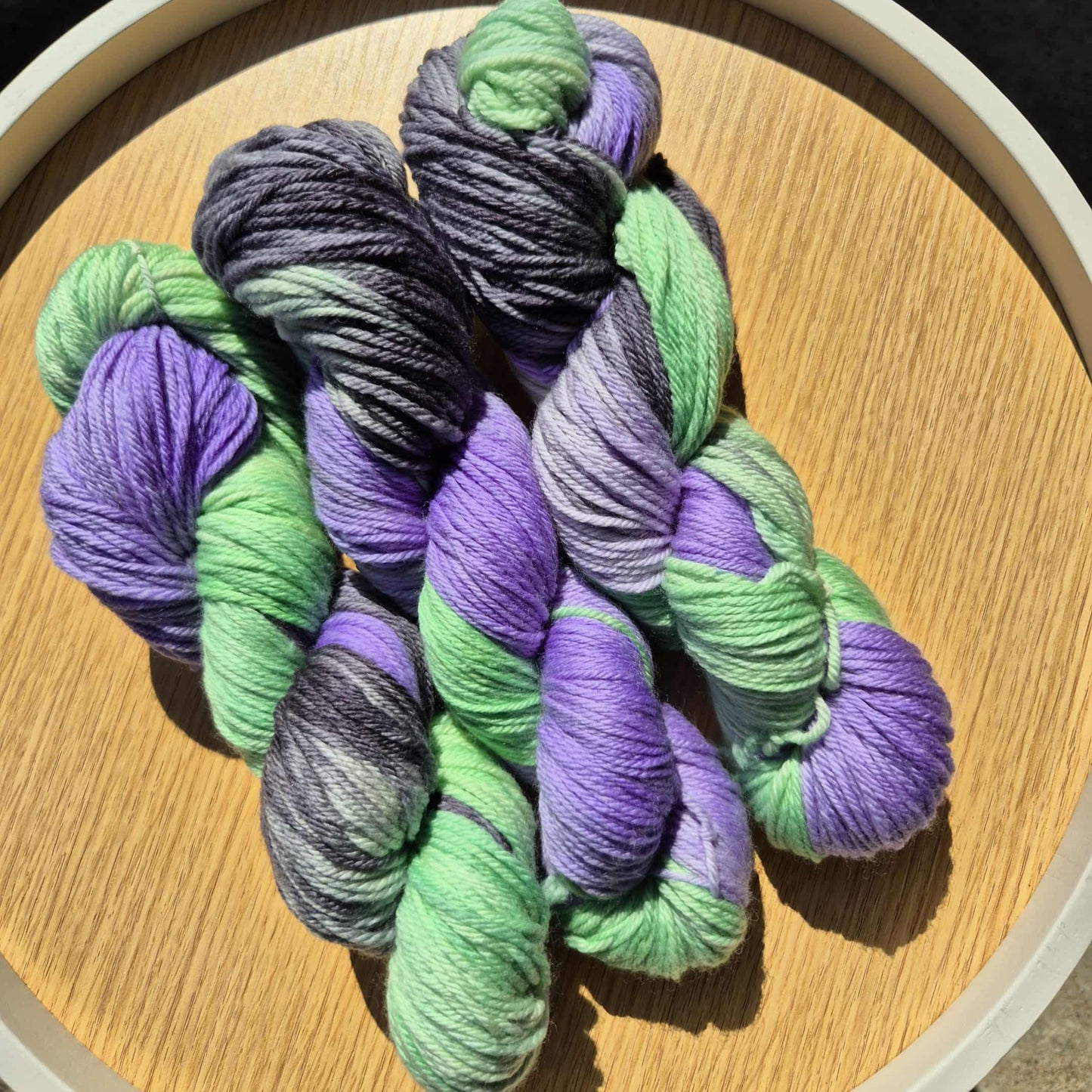 Three skeins of green, purple and black Merino on a wooden board