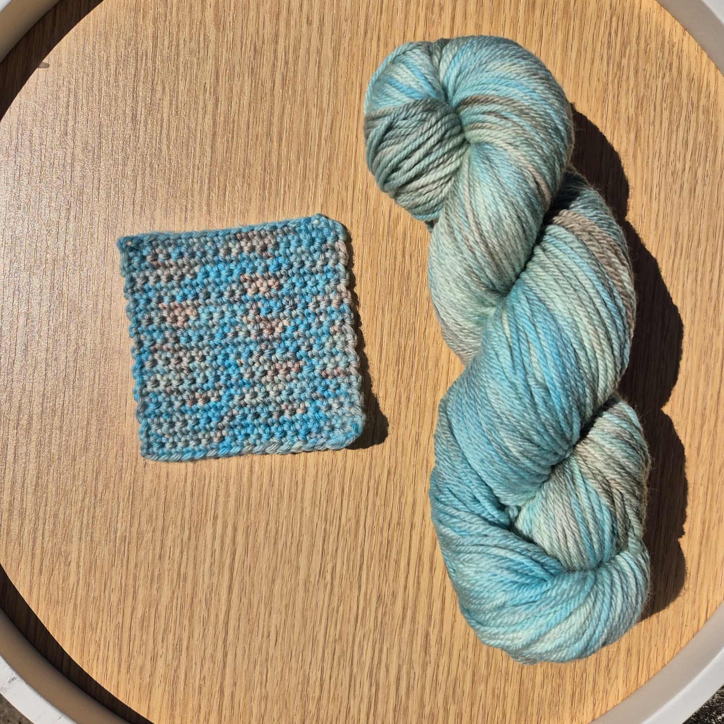 Blue and brown skein of yarn with a crochet swatch on a wooden surface