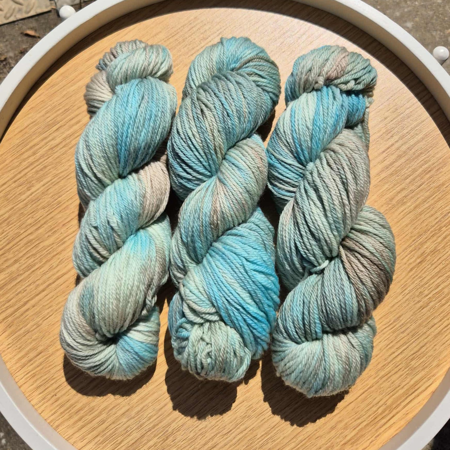 Three skeins of blue and brown yarn on a wooden board with a white rim.