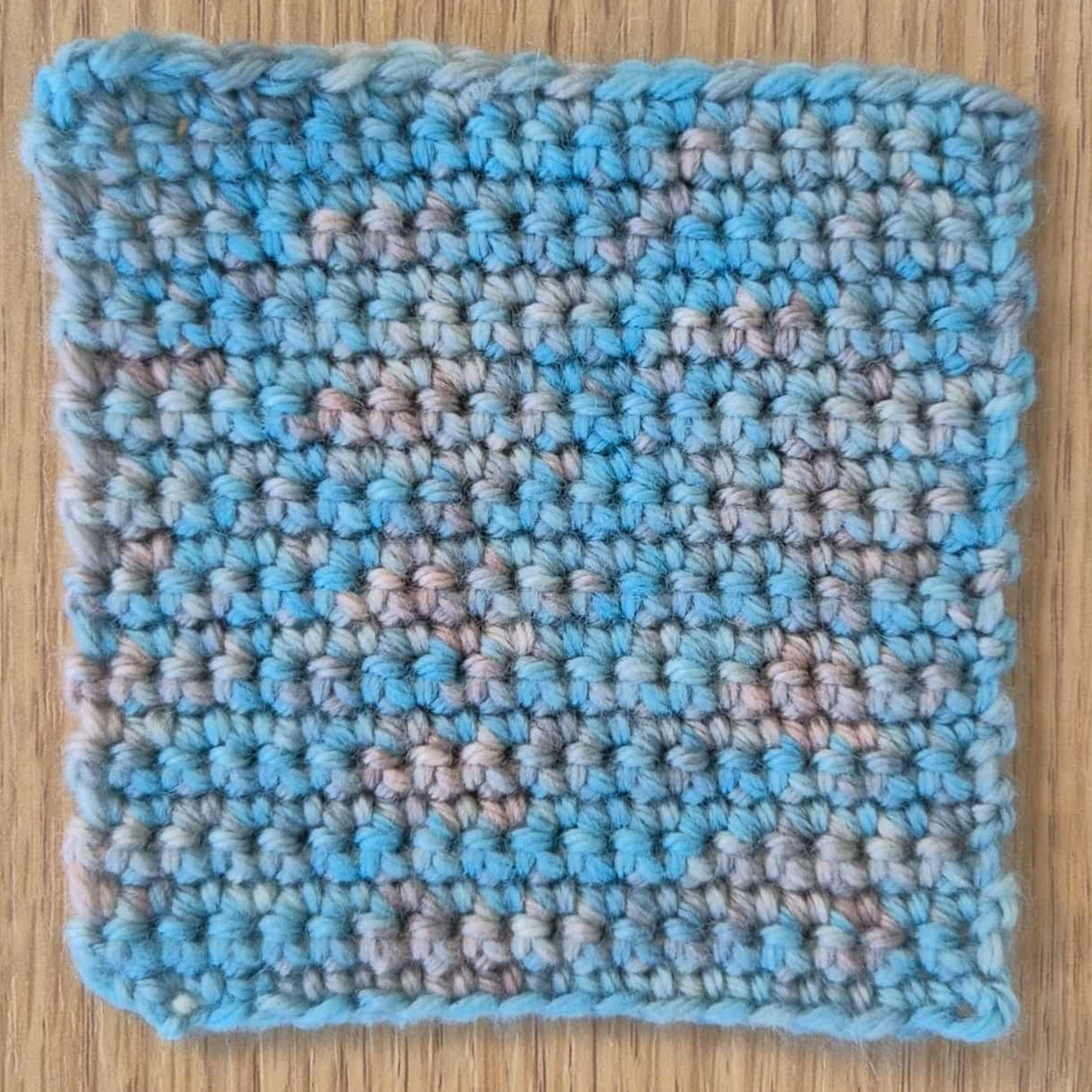 Crocheted square with blue and beige pattern on a wooden surface